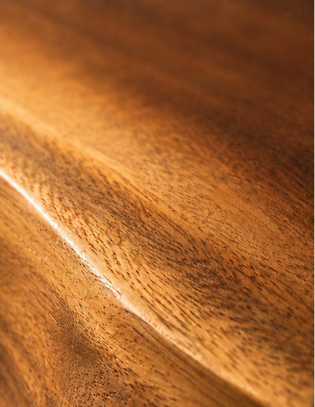 Close-up of the sculpted live edge on a suar wood shelf, showing ripples of golden grain