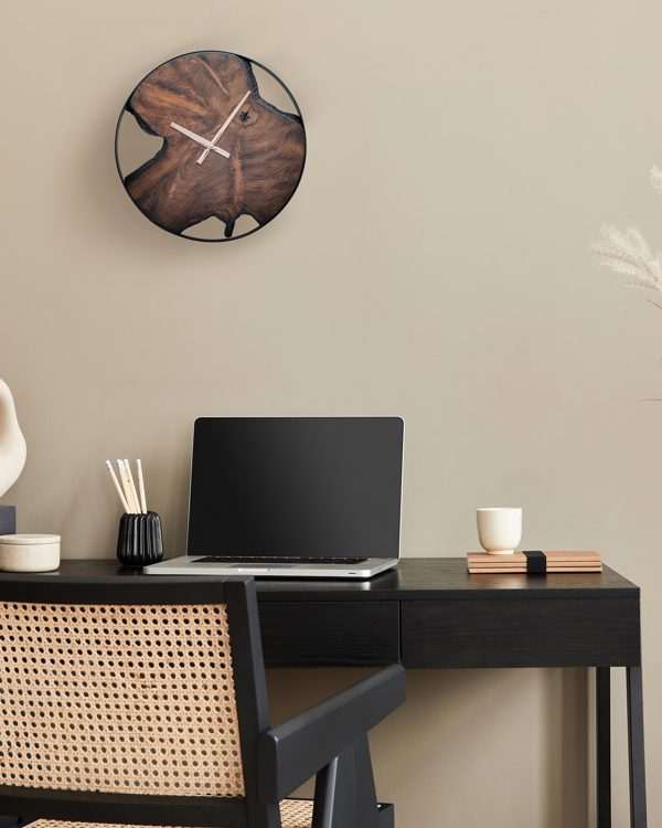 Teak wall clock above a black desk with a laptop and rattan chair in a calm home office
